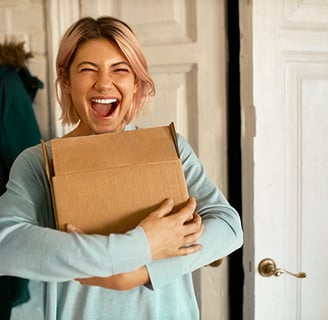 Mulher feliz e sorridente segurando uma caixa, parecendo ser um produto recém-entregue.