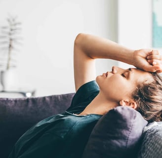 a woman is laying on a couch suffering with pain