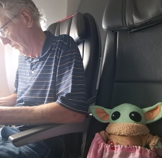 Man in airplane seat with a little green companion in seat next to him