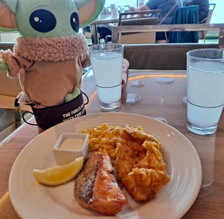 Little green companion beside a plate with salmon and a piece of fried chicken