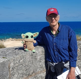 Man standing against low wall holding a little green companion with ocean in background