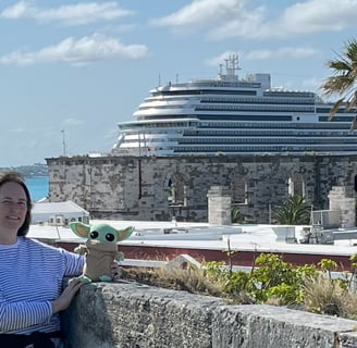 Woman standing by low wall holding a little green companion with cruise ship in background