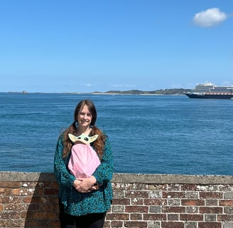 Woman standing in front of low wall with cruise ship in background