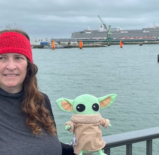 Woman holding little green companion standing at bridge with cruise ship in background