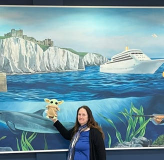 Woman holding little green companion in front of mural of white cliffs of Dover