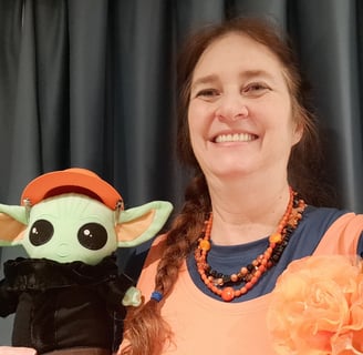 Woman wearing orange shirt holding a little green companion wearing an orange hat