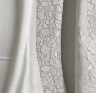 A white lace wedding or bridal dress is hanging on a black hanger in front of a blue trash bin. The dress includes intricate lace details and layered fabric. A tag with an image of a model wearing a similar garment is attached to the hanger.