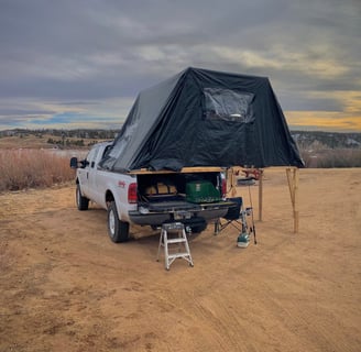 A truck with a fold-out overland tent on it's bed beside a lake