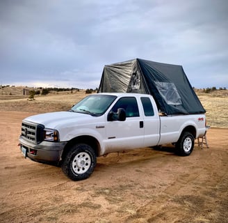 A truck with a fold-out overlanding tent on it's bed on a dirt road
