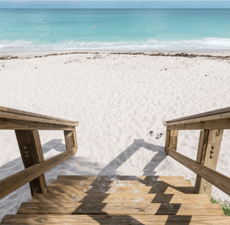 Escalier en bois face à une plage de sable blanc et vue sur la mer