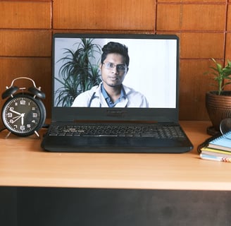 a laptop computer screen showing a doctor's face on a desk