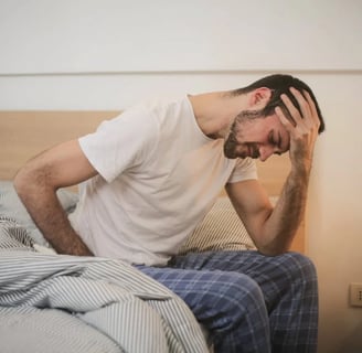 a man with a beard and glasses sitting on a bed