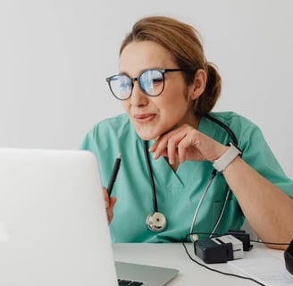 a woman in a green scrubsuit and glasses is looking at a laptop