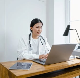 a woman in a white lab coat and a stethoscope on a laptop