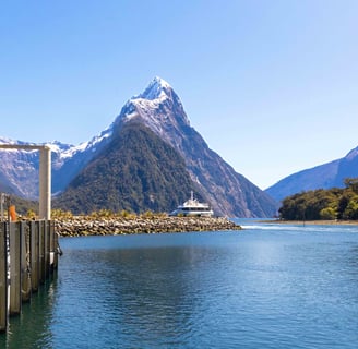 Mitre Peak reflecting in the tranquil waters of Milford Sound, surrounded by clear blue skies.