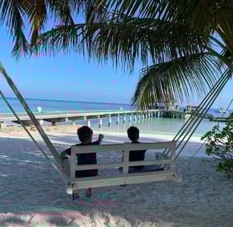 two people sitting on a swing chair in the sand
