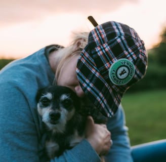 person hugging and kissing dog in a field with pink sunset
