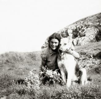 a woman is sitting on a hill with a dog