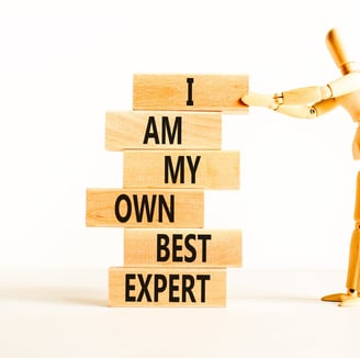 figure holding a pile of wooden blocks. Word on blocks spell I Am My Own Best Expert