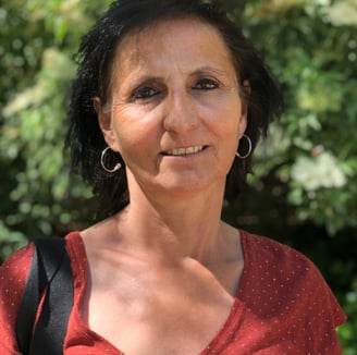 Portrait de Muriel Renucci, avec un fond végétal flou, créant une atmosphère naturelle et apaisante