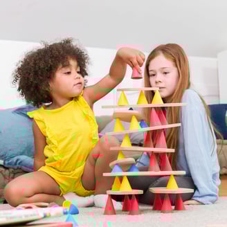 Two children creating a structure from colorful silicone cones and wooden tables in the room