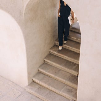 A woman wearing a black top and clacks, carrying a notebook, walking down a marble stairway.