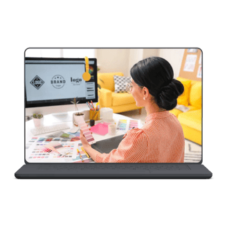 Woman in checked shirt reviewing color swatches while designing graphics on laptop in a cozy workspace.