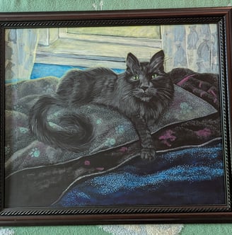 Cherry oak framed arcrylic portrait painting of a long haired black cat with very green eyes laying in his blanketed bean bag