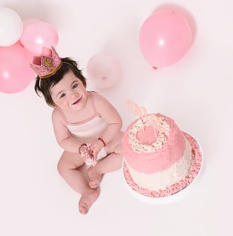 a baby girl sitting near a cake