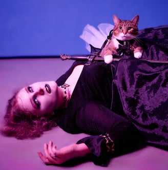 a girl in a black dress dying on the ground with a cat holding a sword on top of her body