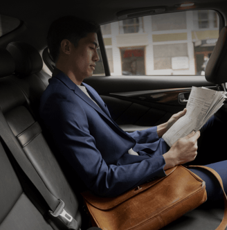 a man in a suit is sitting in a car reading a newspaper