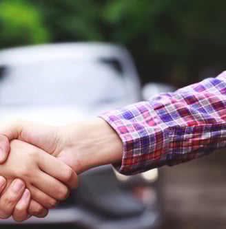two people shaking hands with a car in the background