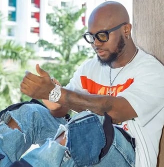 King Promise in a white shirt and blue jeans trousers.