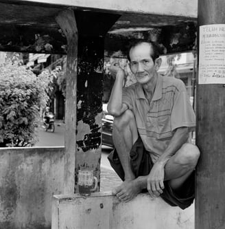 Indonesian man taking a rest, sitting on a wall, smoking