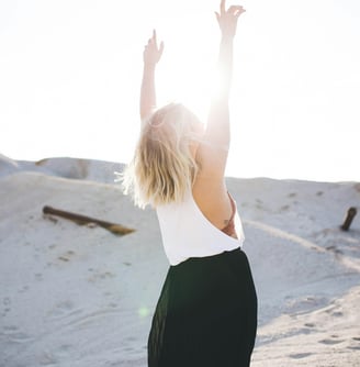 Une femme debout dans le sable, les bras levés, symbole de liberté et de bien-être
