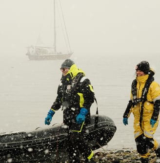 People in a snowy beach with a dinghy and a sailing yacht in the background | Ski and sail in Lyngen