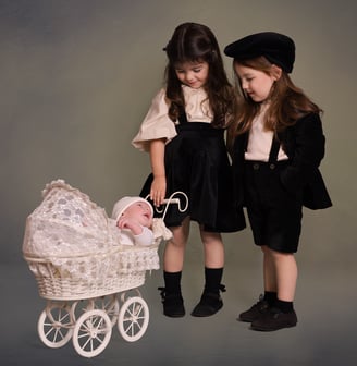 two kids in black dresses and hats are standing next to each other looking at baby
