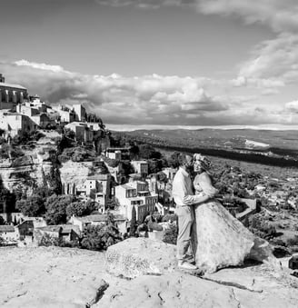 Wide black and white couple photo — kiss on the cheek with panoramic view over Gordes, Provence