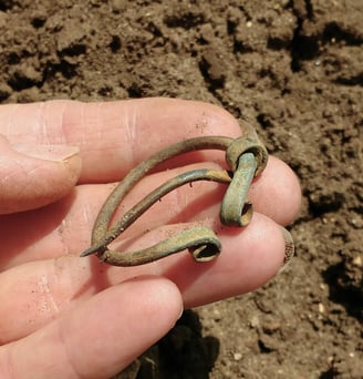 A bronze, circular Iron Age brooch held in the hand of the finder.