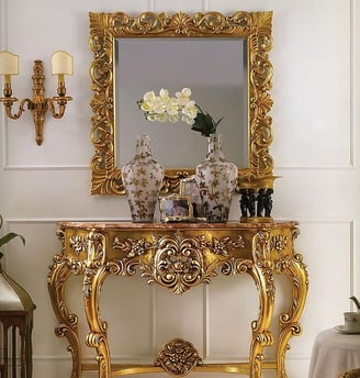 a gold console table with a mirror and a vase with flowers
