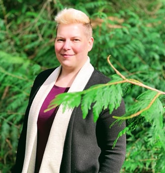 A woman in a black cardigan and jeans standing in front of trees