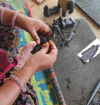 "Tribal artisan shaping wax mold to cast brass idol in traditional lost-wax method"