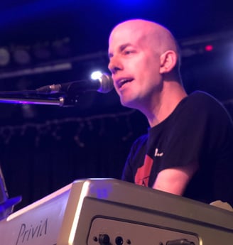 Yoav Rokach Penn wearing a black T-Shirt, Playing the piano and singing in front of a microphone.