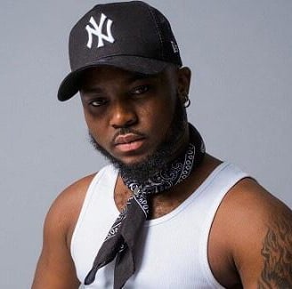 King Promise in a black cap in a singled with a black bandana around his neck.