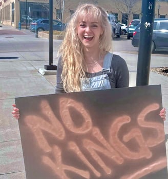 India May holds a sign that says NO KINGS and laughs at a protest
