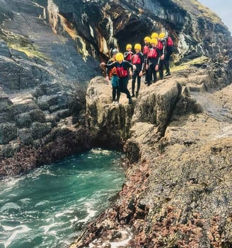 a group of people standing on a cliff side coasteering