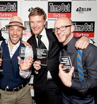 a group of men standing around celebrating winning 3 awards at an event