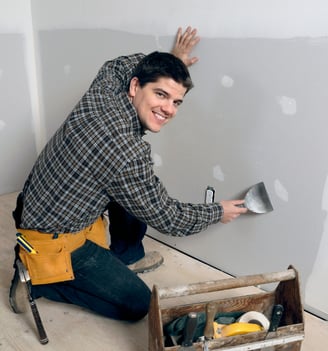 a handy man is smiling and repairing a drywall