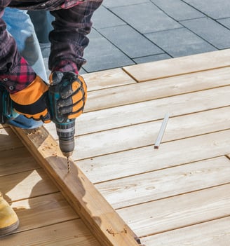 a handyman using a cordless drill to drill in a wood deck