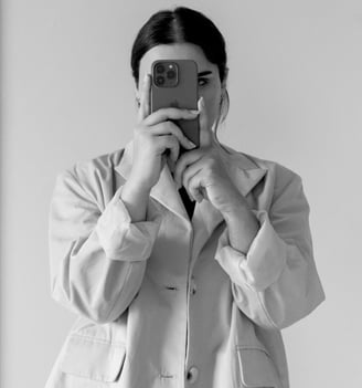 A brunette woman looking at herself in the mirror while taking a selfie on her iPhone